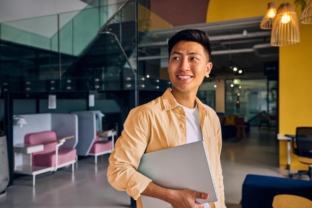 Young asian freelancer smiling and holding laptop in modern office